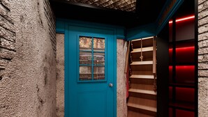 Une porte de couleur bleu-vert avec une fenêtre, un escalier en bois et une bibliothèque éclairée de lumière rouge.