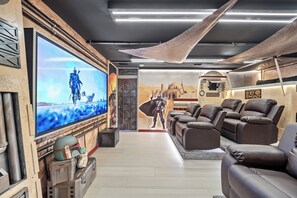 Ein modernes Wohnzimmer mit einem großen Flachbildfernseher, Ledersofas und einer Wand im Star Wars-Design.
