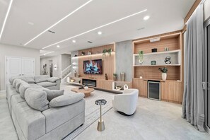 A modern living room with a grey sectional sofa, a flat-screen TV, wooden shelving, and a built-in fireplace. - 10BR house sleeps 27 near Disney (Clermont)
