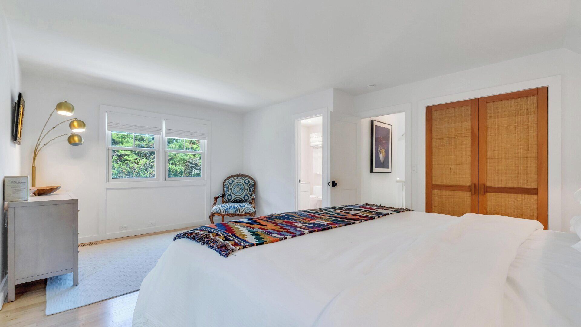 Une chambre à coucher avec un grand lit, une chaise, un bureau, une lampe et une armoire.