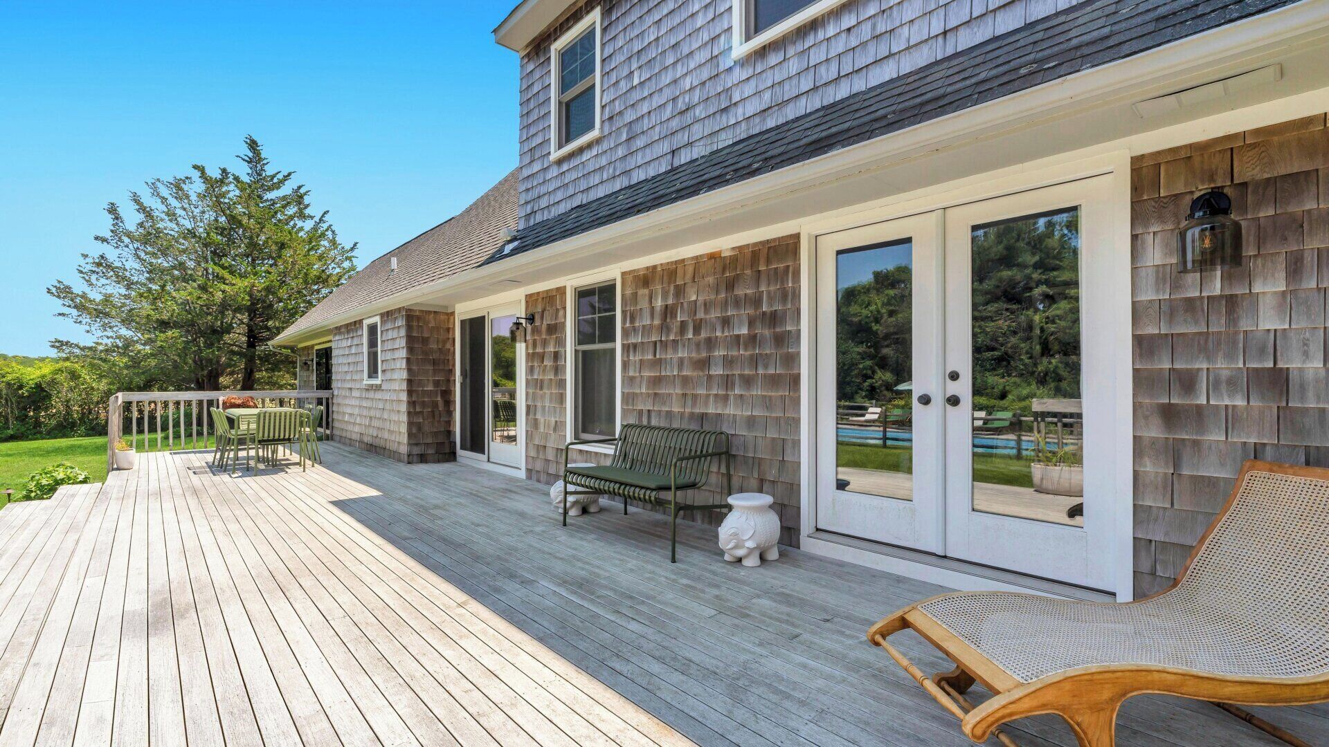 Une terrasse couverte avec des meubles d’extérieur, une piscine et une maison dont la façade est recouverte de bardeaux.