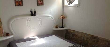 A bedroom with a large bed, a nightstand, a wall-mounted lamp, and a window with a zebra-patterned curtain.