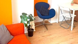 A room with a blue chair, a white table, a potted plant, and an orange sofa. - Ground Floor Studio - Willesden Green - Sleeps 4 (London)