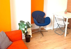 A room with a blue chair, a white table, a potted plant, and an orange sofa. - Ground Floor Studio - Willesden Green - Sleeps 4 (London)