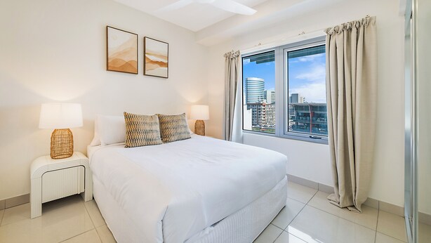 Una camera da letto con un letto grande, due comodini con lampade, una ventola a soffitto, una finestra con tende e due opere d'arte appese al muro.