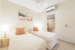 A hotel room with two beds, a ceiling fan, an air conditioning unit, and a bathroom visible through an open door. - Capital Panorama Central City Escape w Pool and Gym (Darwin)