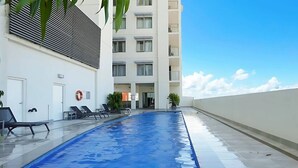 Una piscina con lettini, un edificio con balconi e cielo sereno.
