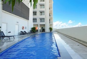 A swimming pool with lounge chairs, a building with balconies, and a clear sky. - Capital Panorama Central City Escape w Pool and Gym (Darwin)