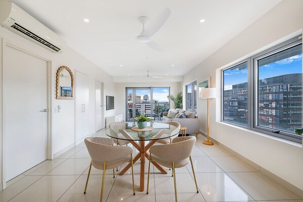 Un espace repas moderne avec une table en verre, quatre chaises et un ventilateur de plafond.