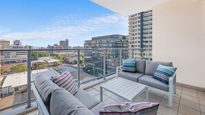 Un balcone con una divano e un tavolo, vista su una città con edifici moderni.