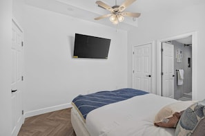 A bedroom with a bed, a ceiling fan, a mounted TV, and a door leading to a bathroom. - The Banana Cabana - Cozy Cottage (West Palm Beach)