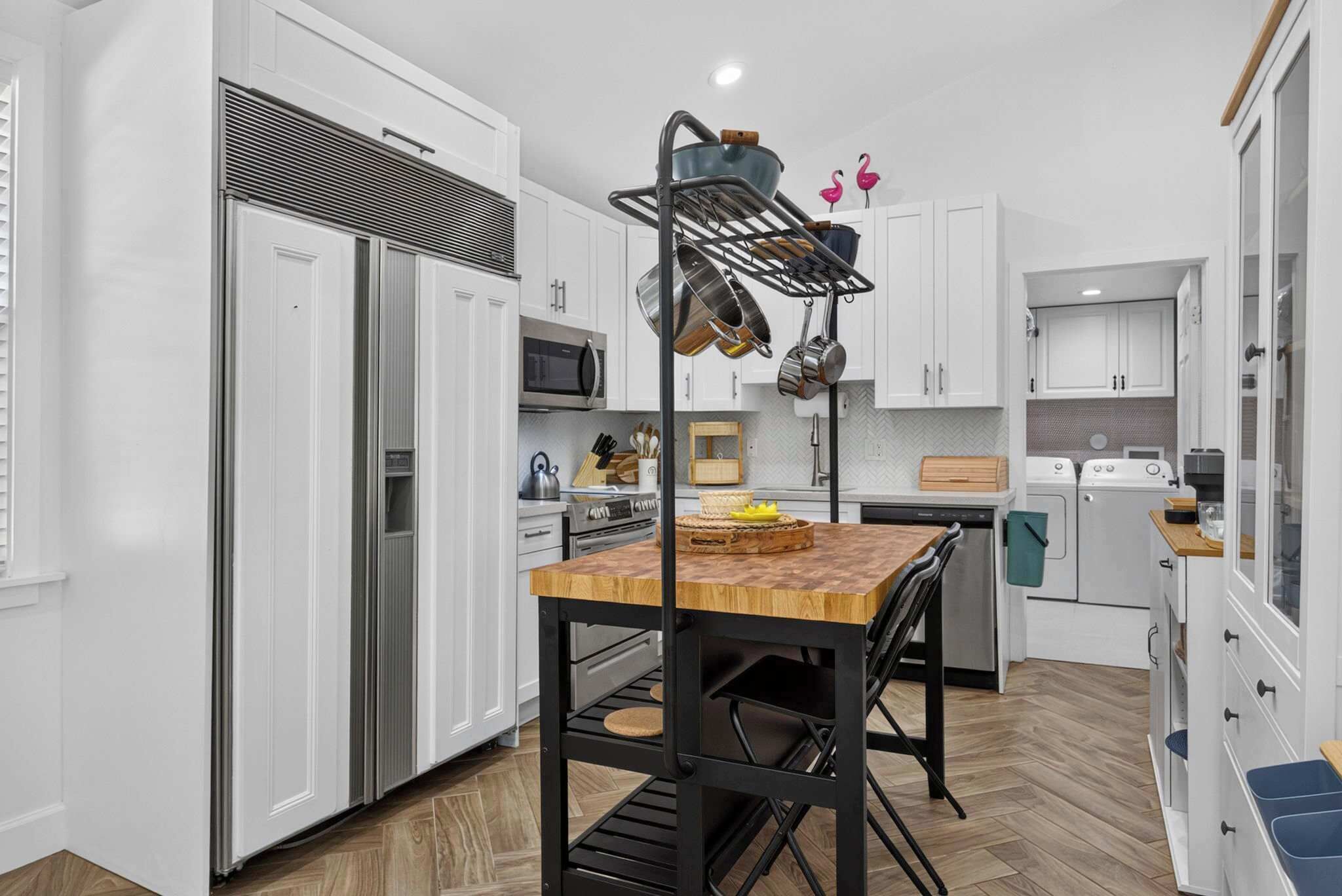 A modern kitchen with white cabinetry, stainless steel appliances, and a wooden dining table.
