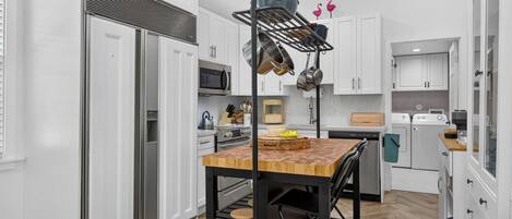 A modern kitchen with white cabinetry, stainless steel appliances, and a wooden dining table.