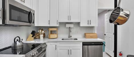 A modern kitchen with white cabinets, stainless steel appliances, and a herringbone tile backsplash.