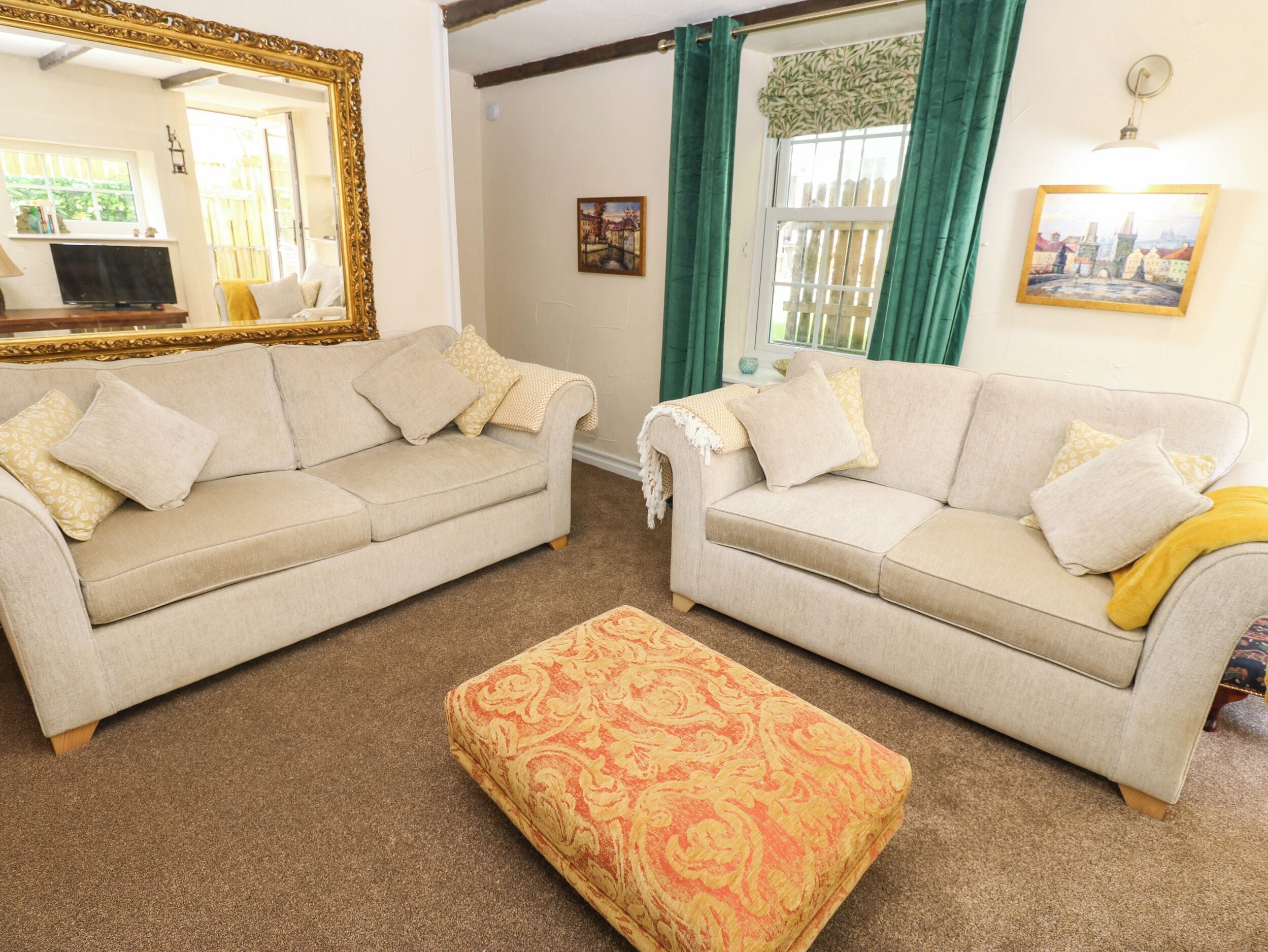 A living room with two sofas, a patterned ottoman, a large mirror, and a painting on the wall.
