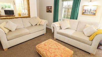 A living room with two sofas, a patterned ottoman, a large mirror, and a painting on the wall.