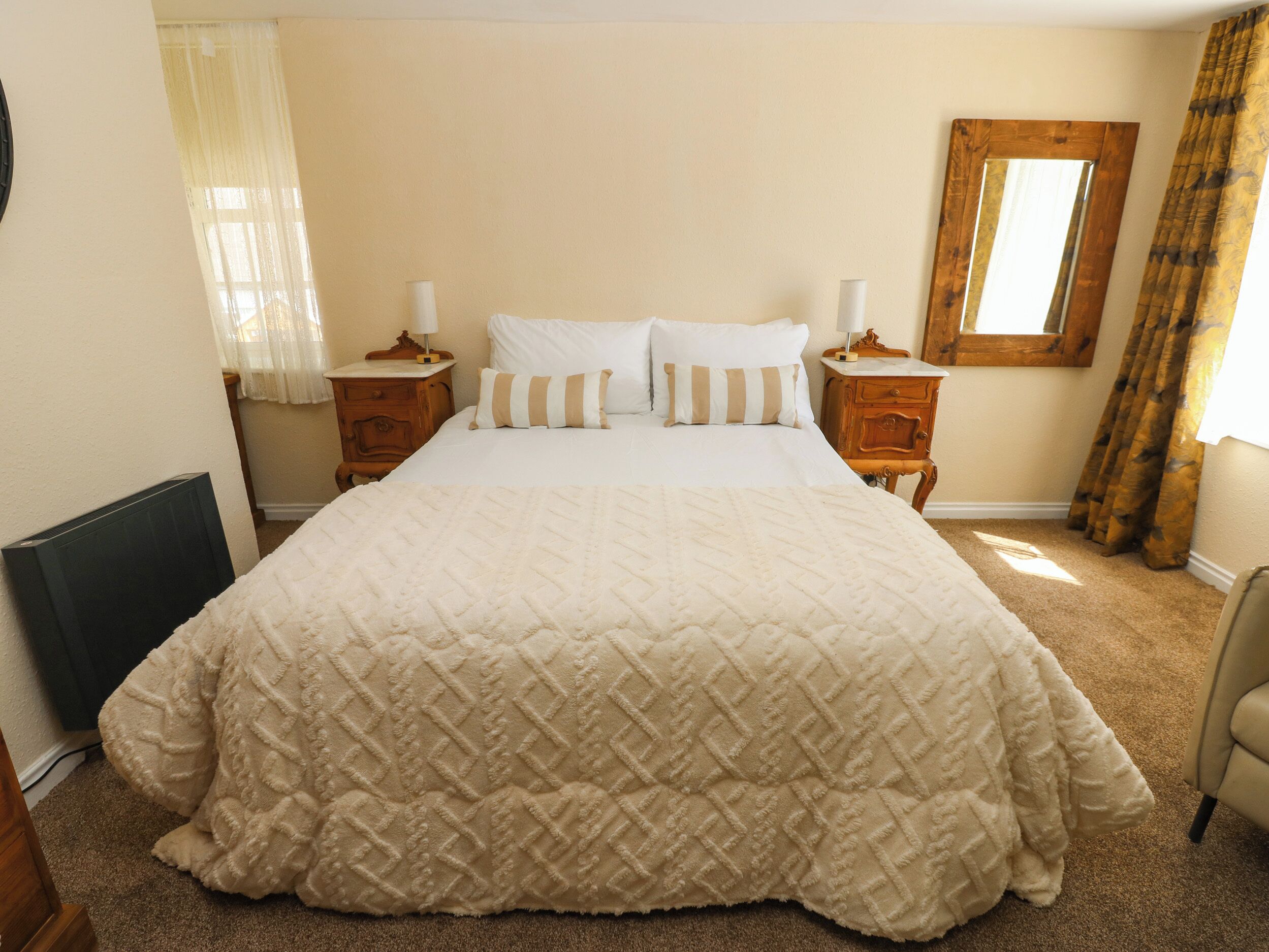 A bedroom with a large bed, two bedside tables, a window with curtains, and a wooden headboard.