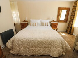 Quarto com cama grande, duas mesas de cabeceira, janela com cortinas e cabeceira de madeira.
