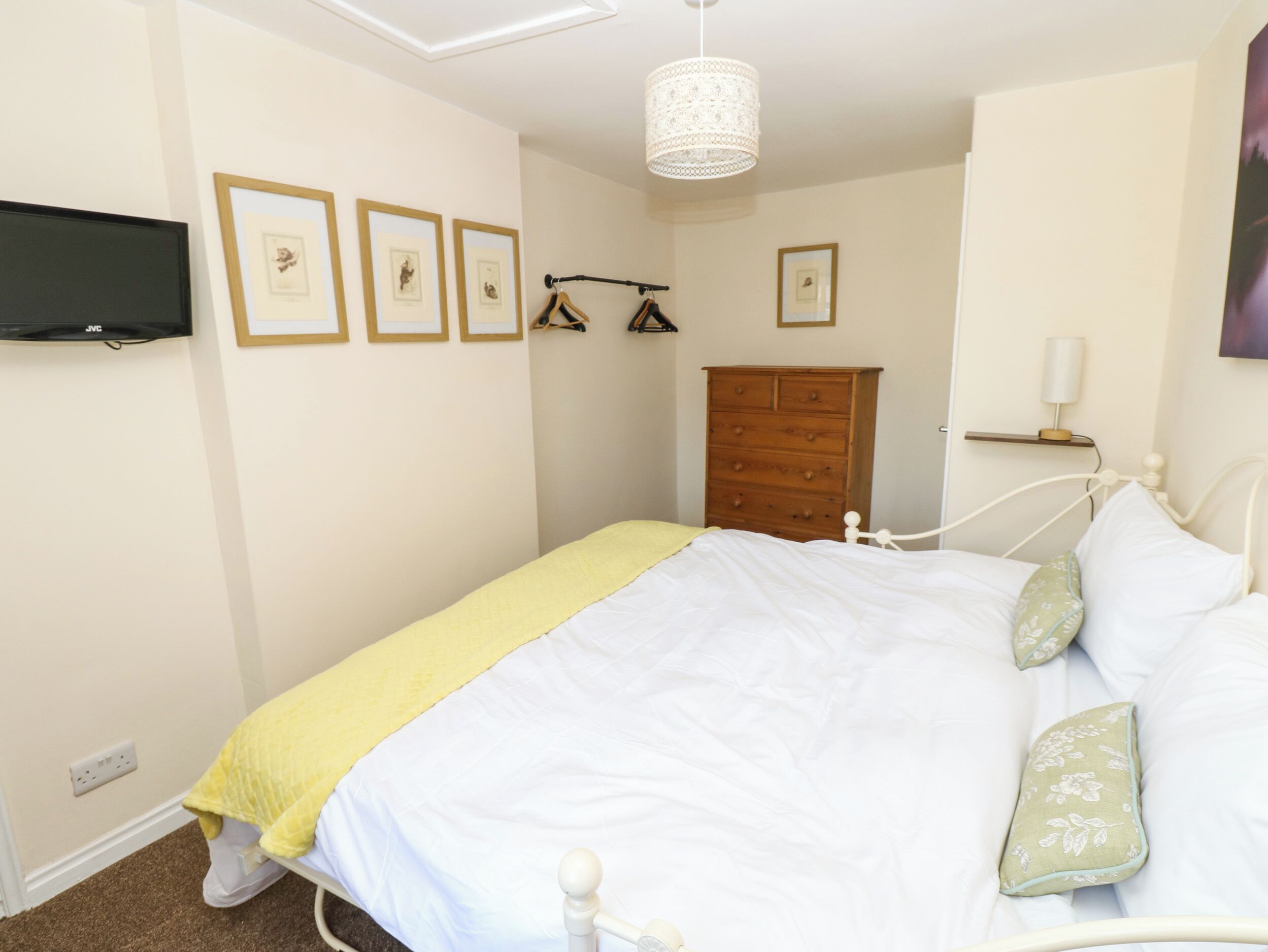 Een slaapkamer met een bed, een dressoir, een televisie en ingelijste foto’s aan de muur.