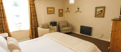 A hotel room with a large bed, a chair, a desk, and a radiator.