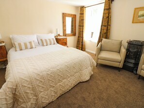 Un dormitorio con una cama grande, una silla, un tocador y un espejo en la pared.
