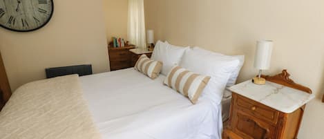 A neatly made bed with a white comforter and pillows, a wooden nightstand with a lamp, and a wall clock.