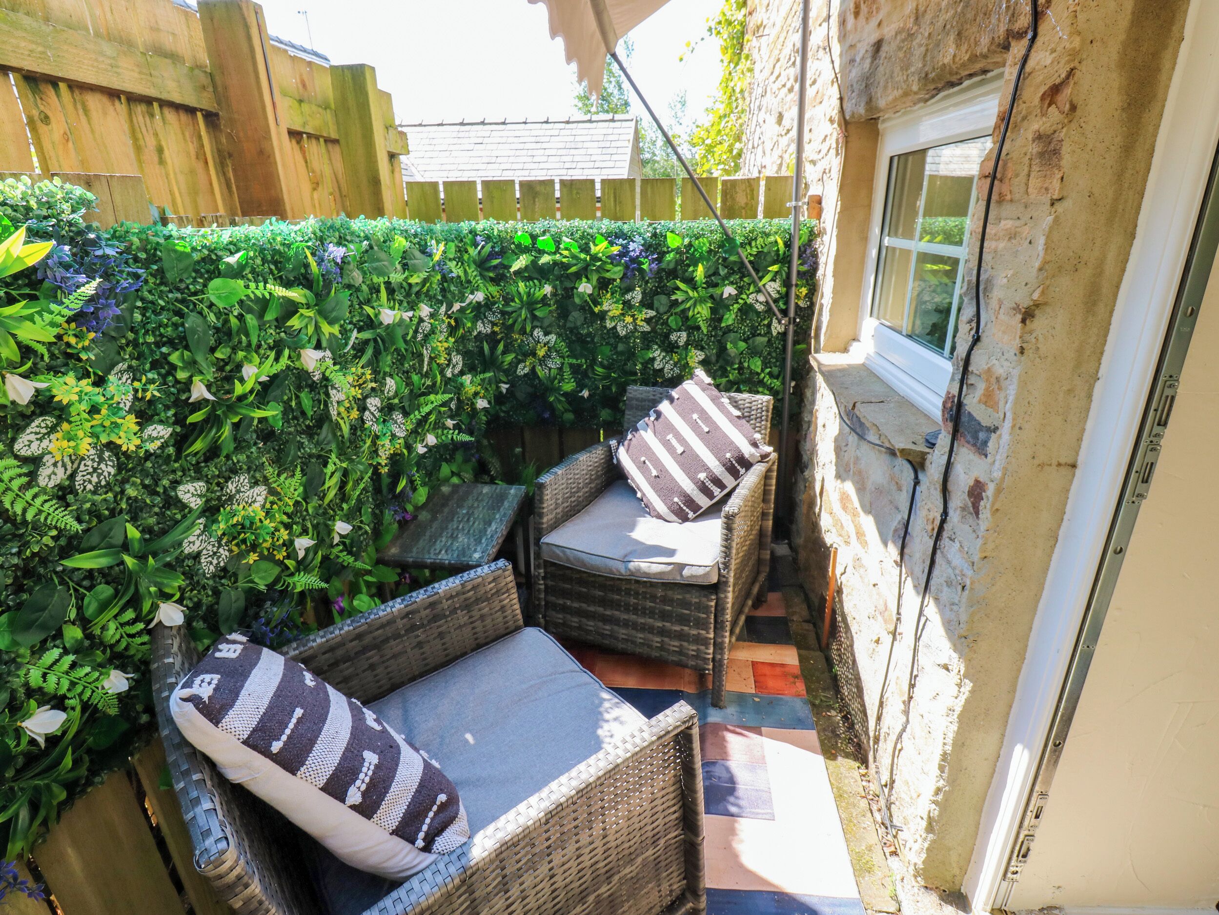 A small outdoor seating area with wicker furniture and cushions, surrounded by dense foliage.