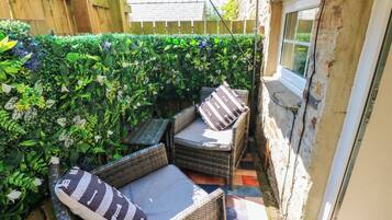 A small outdoor seating area with wicker furniture and cushions, surrounded by dense foliage.
