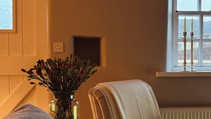 Ein gemütliches Zimmer mit einem gestreiften Sessel, einem kleinen Tisch mit Blumenvase und einem Fenster mit Blick.