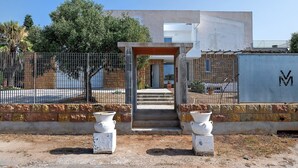 Ein Gebäude mit einer Betonfassade, einem Metallgitter und einem gepflasterten Eingang mit Stufen zu einer Tür.