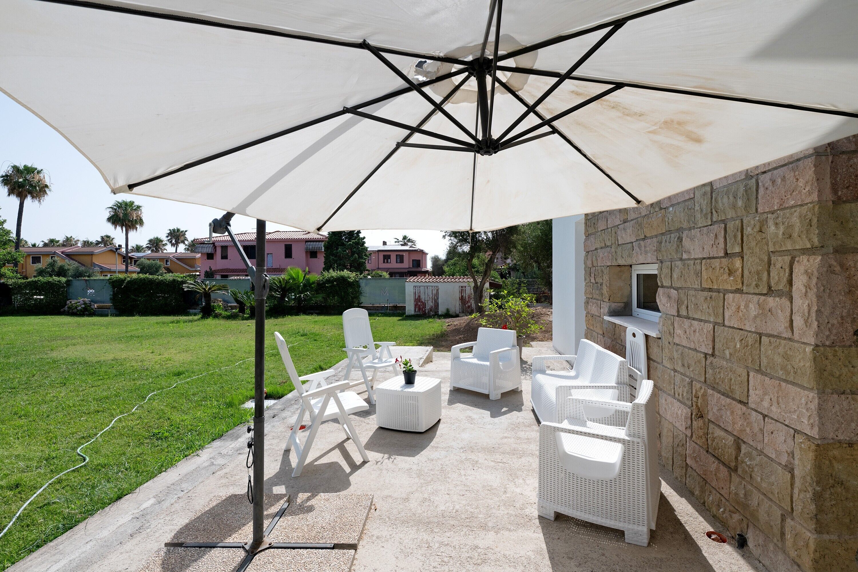 Eine Terrasse im Freien mit weißen Korbmöbeln, einem großen Sonnenschirm und einer Steinmauer.