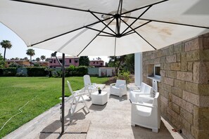 Eine Terrasse im Freien mit weißen Korbmöbeln, einem großen Sonnenschirm und einer Steinmauer.