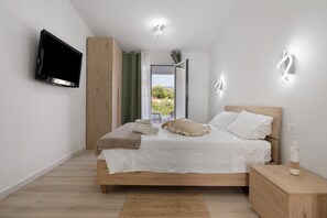 Une chambre à coucher moderne, avec un lit, un téléviseur fixé au mur et une vue sur l’extérieur.