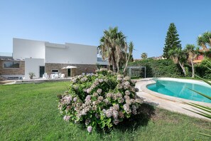 Ein modernes Haus mit Swimmingpool, einer Terrasse mit Gartenmöbeln und einem üppigen Garten.