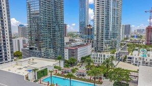 A high-rise building with a rooftop pool surrounded by palm trees and lounge chairs. - Cozy Miami Studio - Pool & Gym - Views (Miami)
