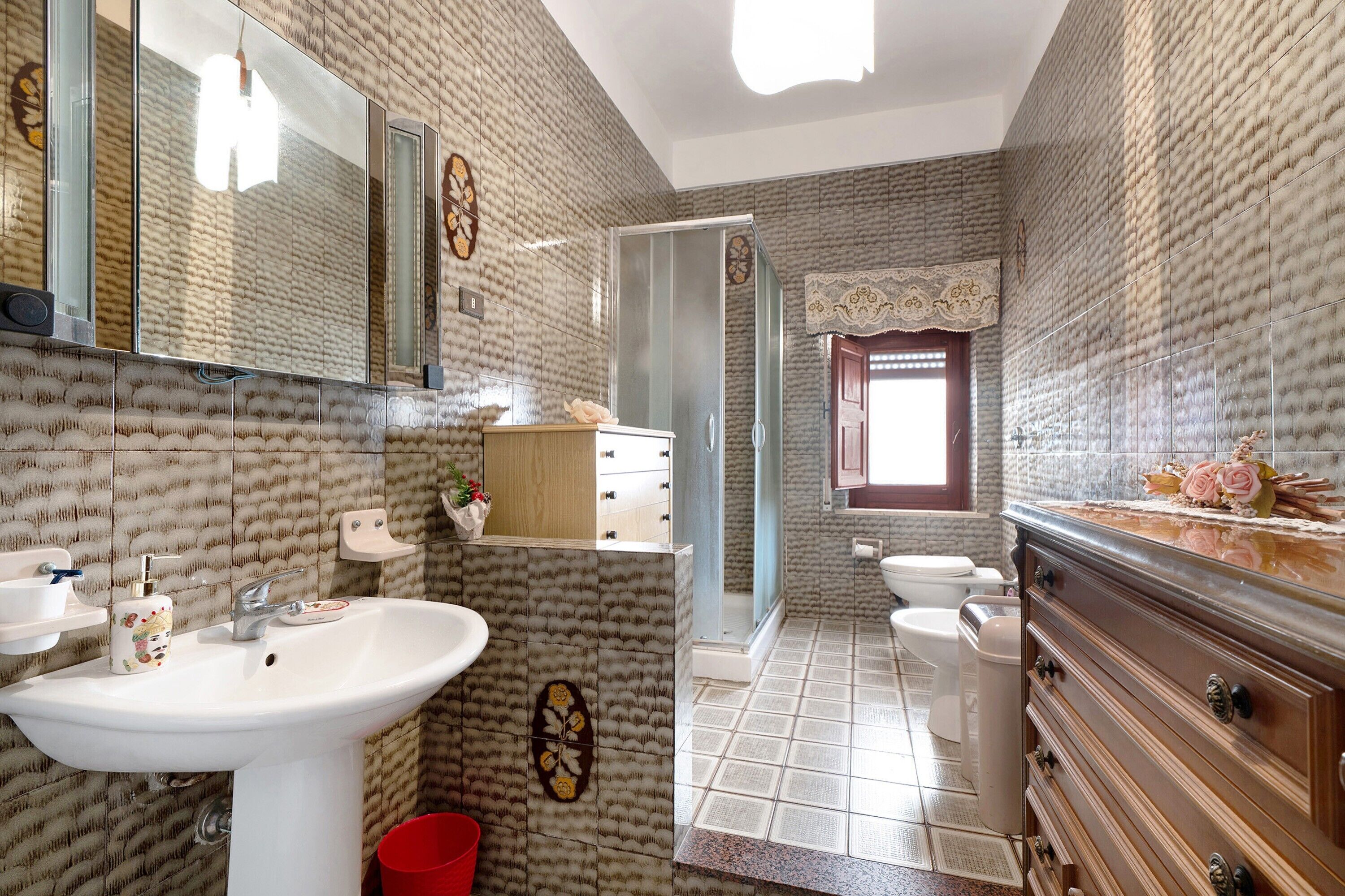 A bathroom with a white sink, a mirror, a wooden vanity, a toilet, and a shower area.