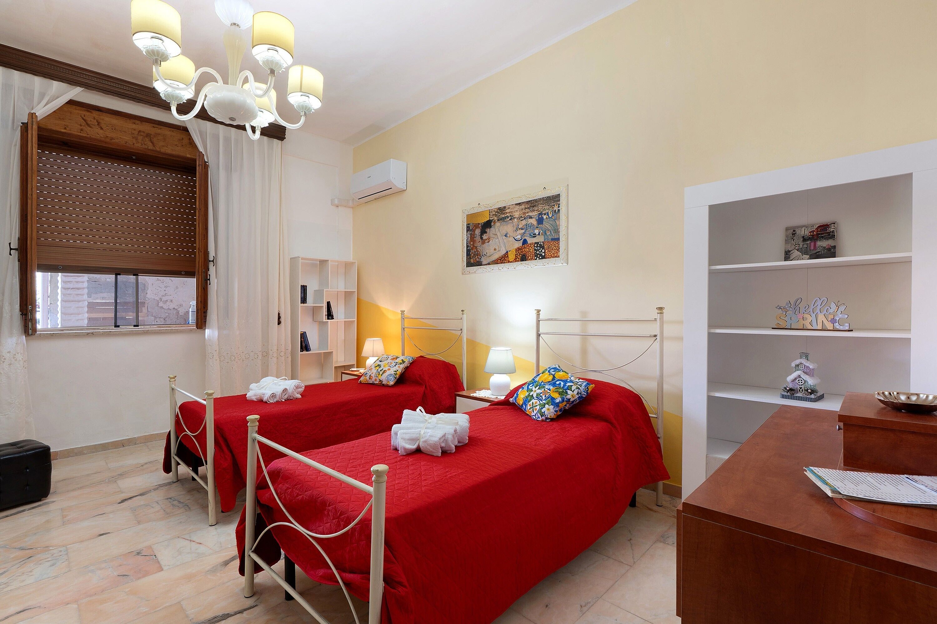 Ein Hotelzimmer mit zwei Betten, einer Chandelüster, einem Gemälde, einem Regal mit Dekoration und einer Klimaanlage.