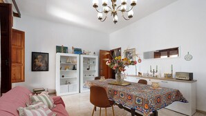 Een eethoek met een tafel voor twee personen, een bank met geplooide kussens en een kroonluchter erboven.