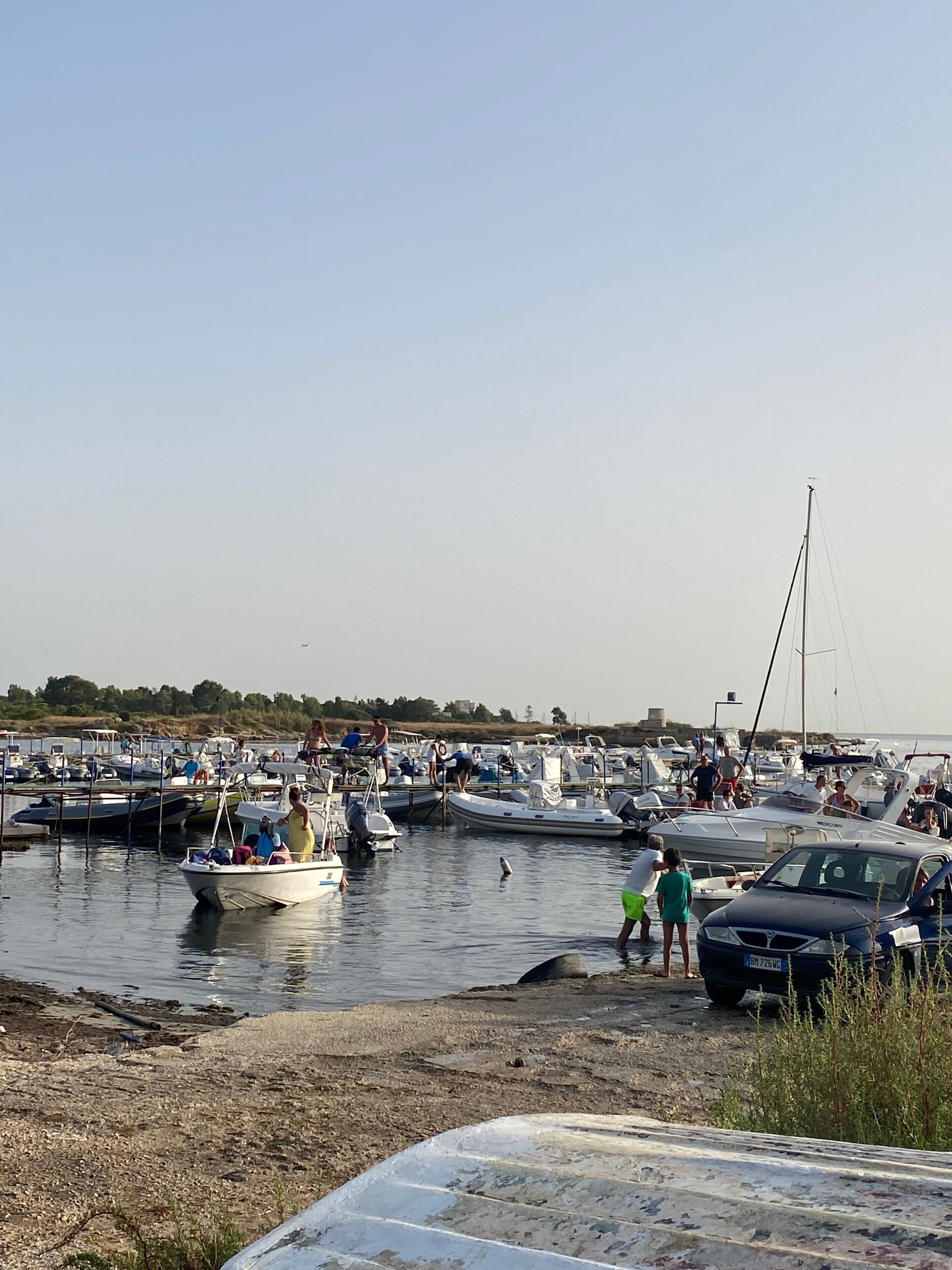 Un port de plaisance avec des bateaux amarrés et des personnes se trouvant près de l’eau.