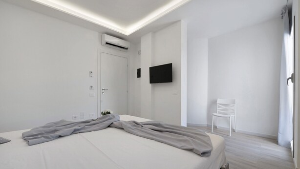 Un dormitorio moderno con una cama, un televisor de pantalla plana, un equipo de aire acondicionado y una silla blanca.