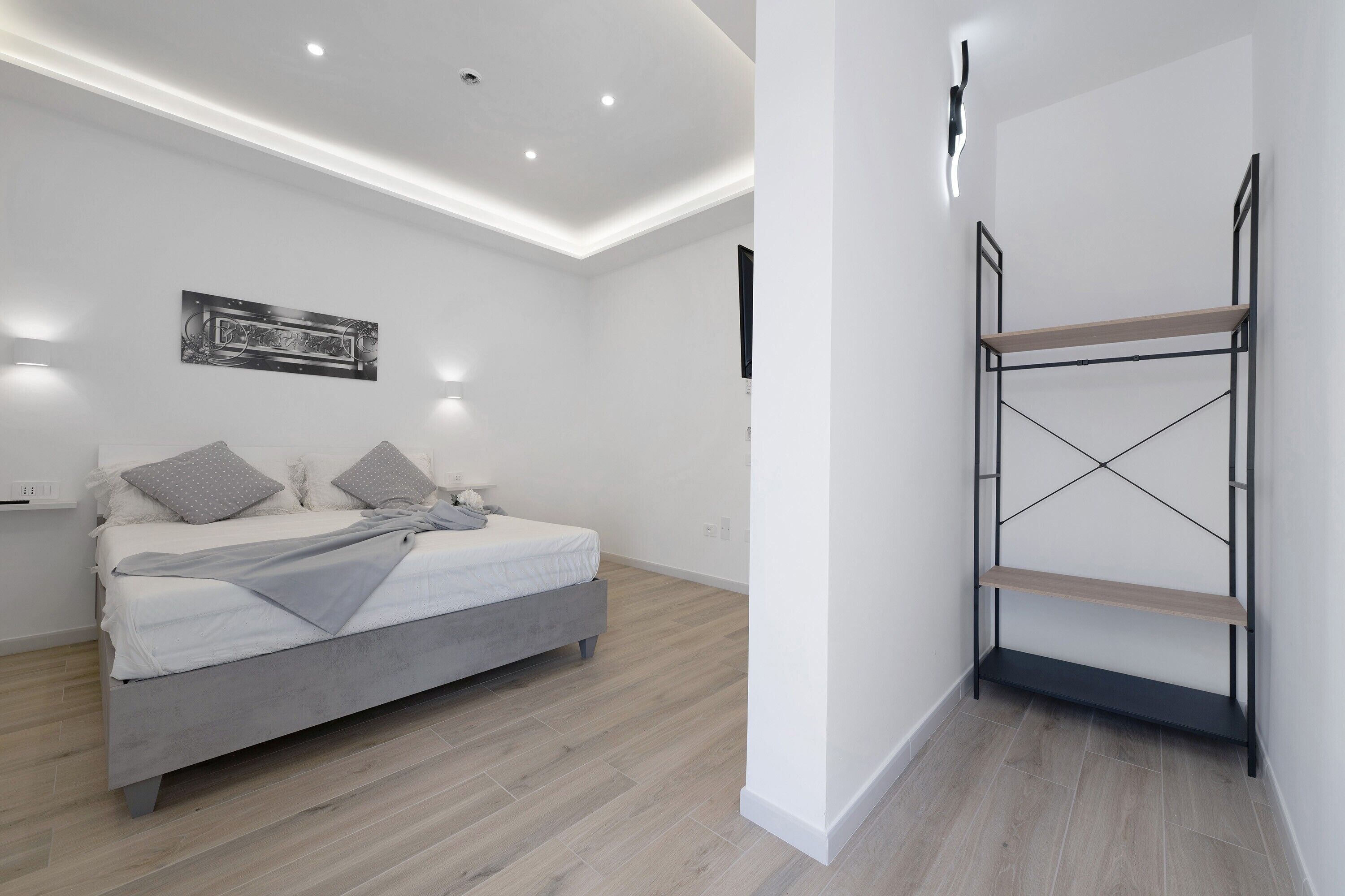 A modern bedroom with a bed, a wall-mounted shelf, and recessed ceiling lighting.