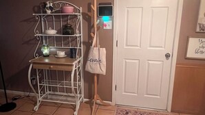 A room with a white door, a metal shelf with kitchen items, a bag on a stand, and a small rug. - Cute and cozy 3 bedroom 2 bath home. Close to TTU and LCU as well! (Lubbock)