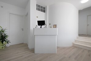 A modern interior with a white reception desk, a potted plant, and a staircase. - Villa Matilde Domo Boutique - Barby Room (Torre degli Ulivi)