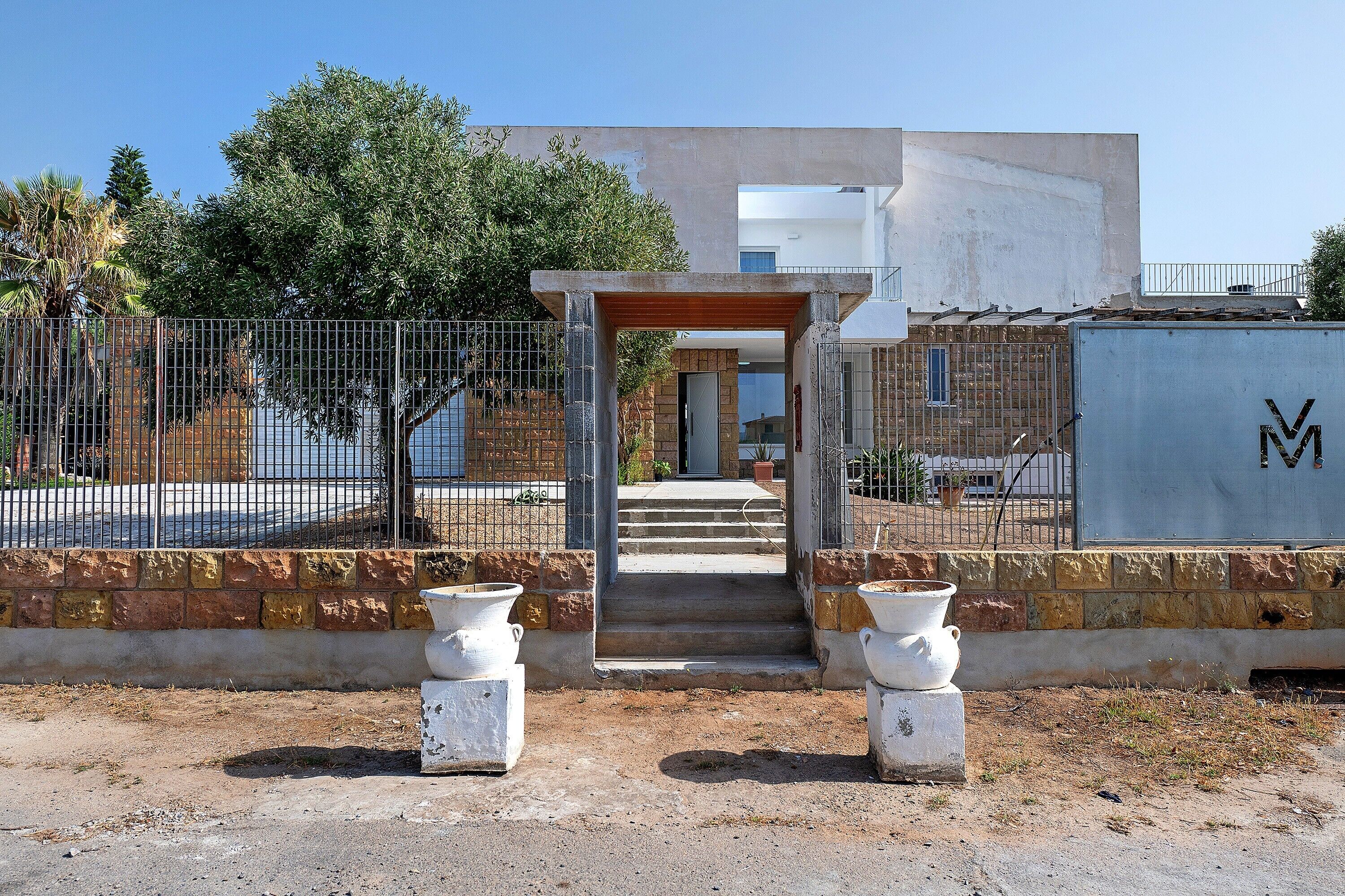 A building with a concrete facade, a metal gate, and a paved entrance with steps leading to a door.