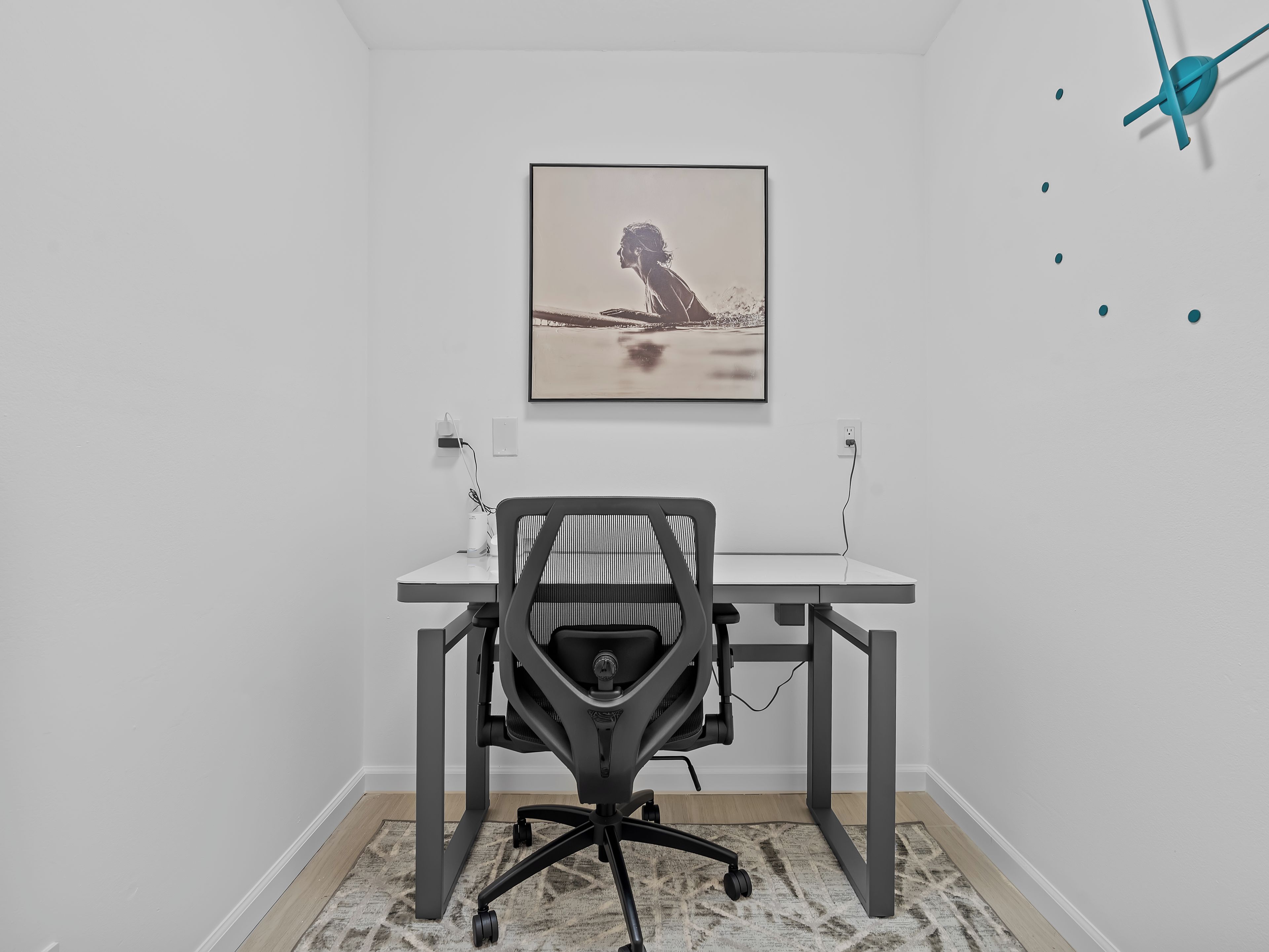 A modern office space with a desk, chair, and a framed picture on the wall.
