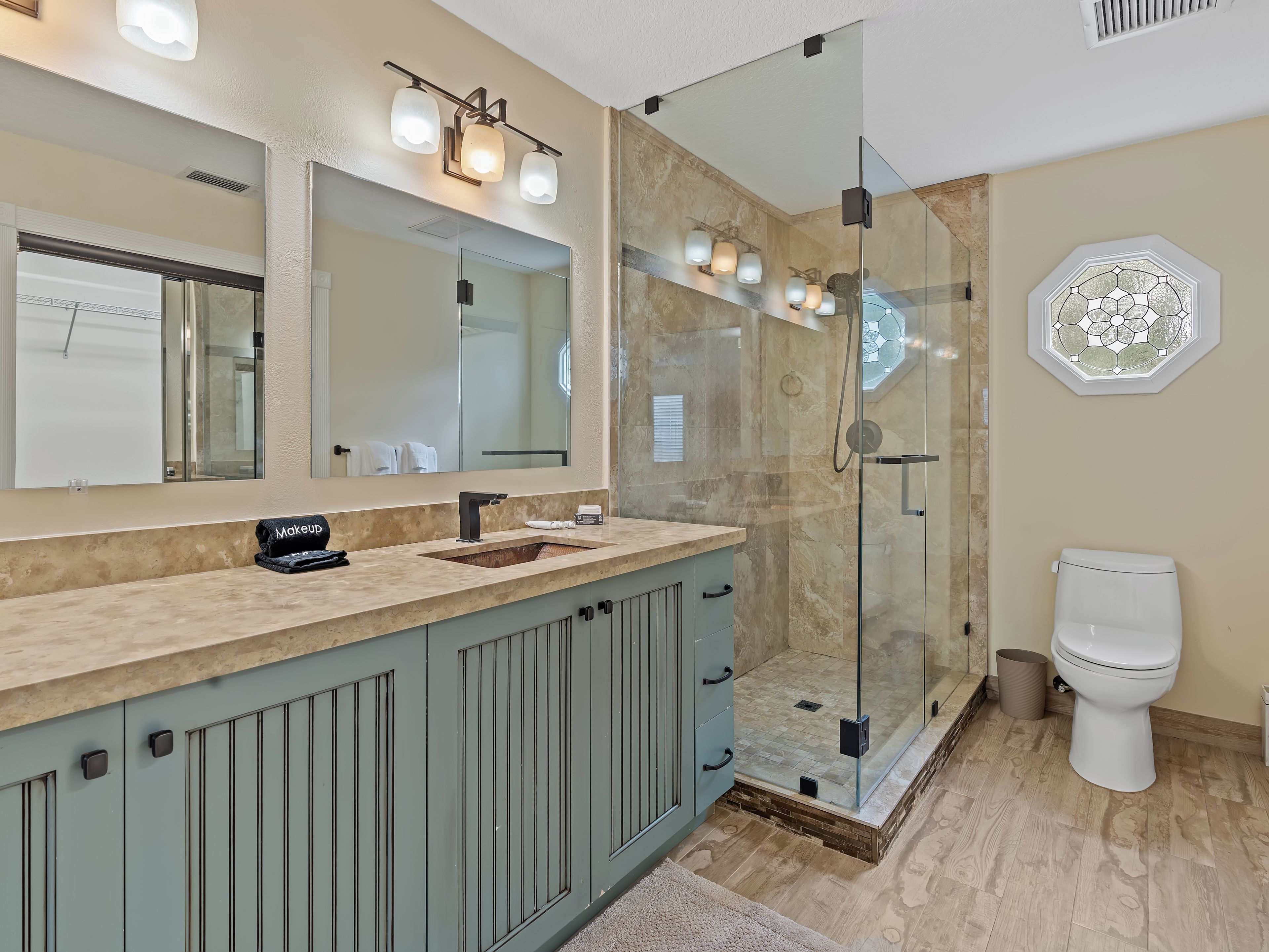 A bathroom with a glass-enclosed shower, a large mirror, and a vanity with a sink.