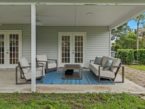 A covered porch with a seating area, including a sofa and two chairs, a small table, and a ceiling fan. - Charming and secluded Jupiter hideaway close to everything!  Pet friendly (Jupiter)