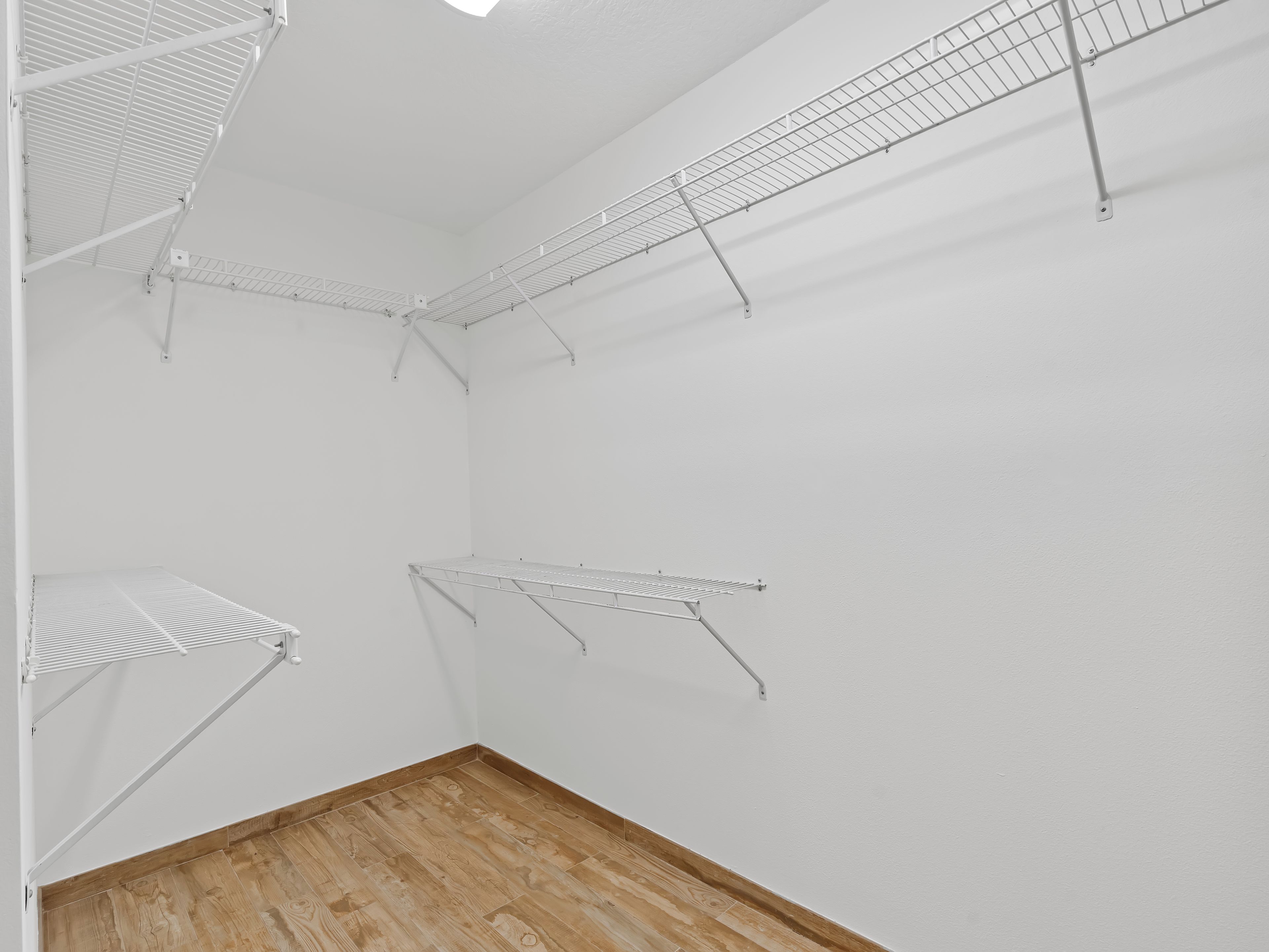 A room with white walls, a wooden floor, and metal wire shelves.