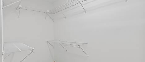 A room with white walls, a wooden floor, and metal wire shelves.