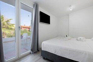 A bedroom with a bed, a TV, and a sliding glass door to a balcony. - Villa Matilde Domo Boutique – Suite Pietra Daniele (Torre degli Ulivi)